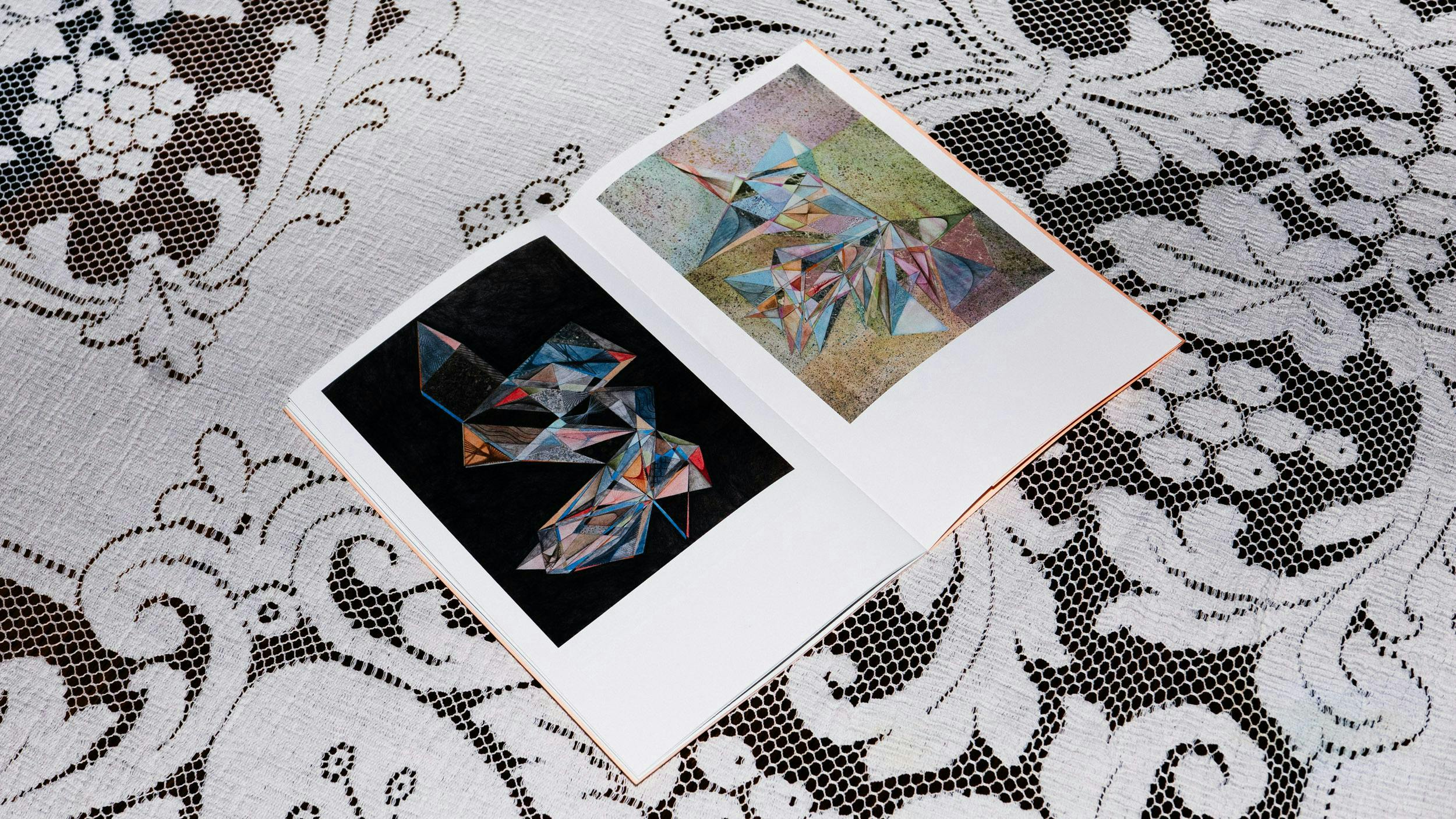 Booklet open on surface with white lace tablecloth, drawings of abstract colourful shapes