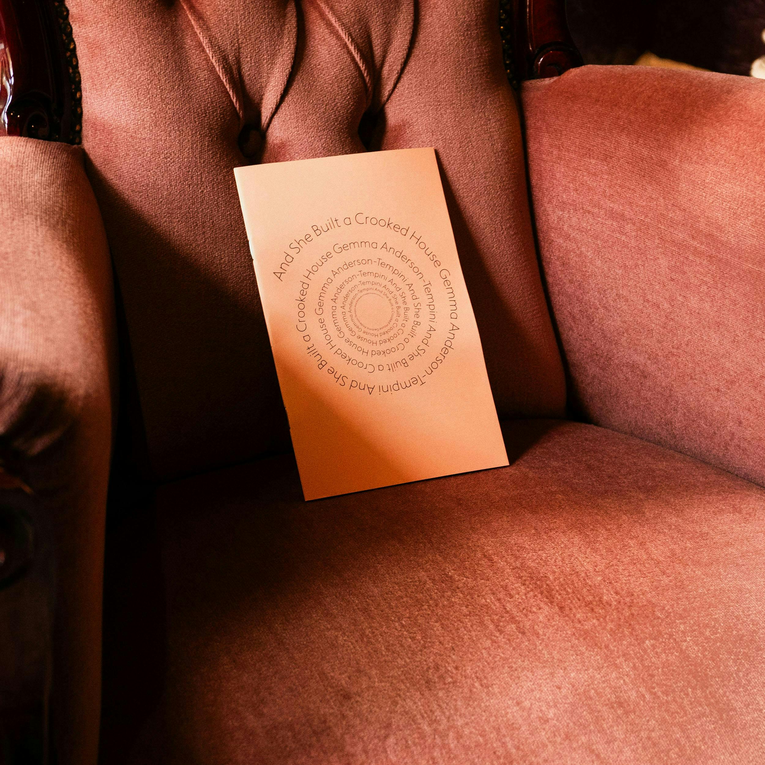 Peach booklet lies on dark salmon velvet chair, spiral text on cover