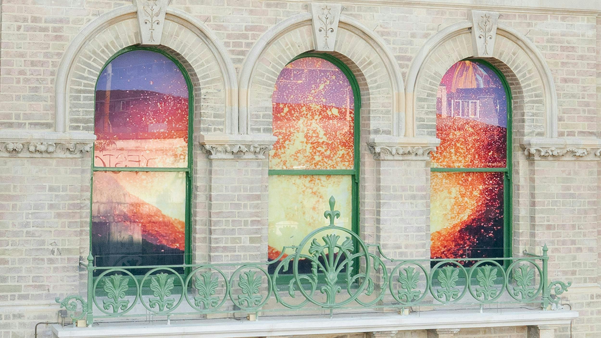 Exterior of old brick building with arched windows, with a vinyl image of a volcano in the windows