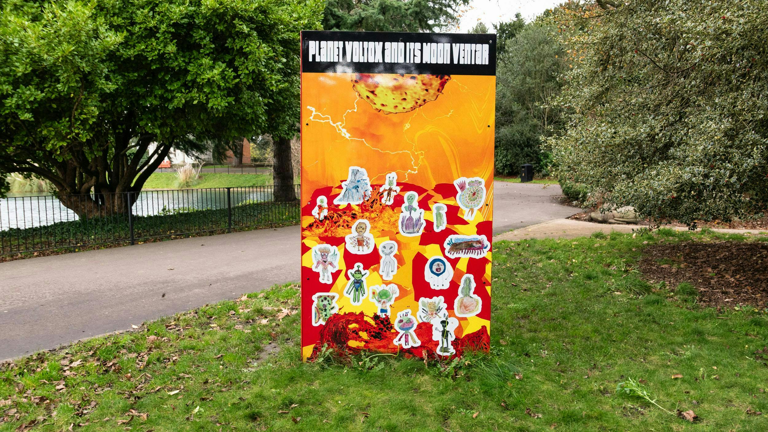 Large orange sign in a green park with 'PLANET VOLTOX AND ITS MOON VENTAR'